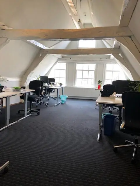 Kantoorruimte op een zolderverdieping aan de Herengracht met houten balken, bureaus en bureaustoelen.