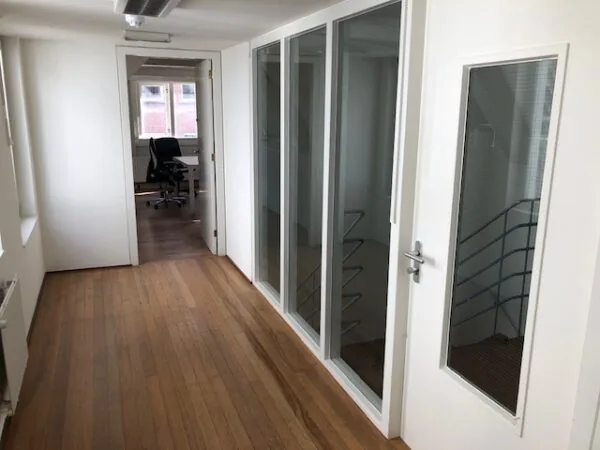 Een lichte kantoorruimte aan de Herengracht met houten vloer, glazen wanden en uitzicht op een werkplek bij het raam.