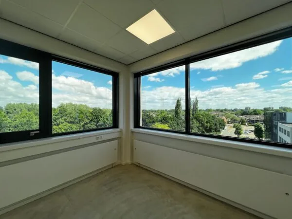 Leeg hoekkantoor met grote ramen en uitzicht op groen en stad aan de Nevelgaarde.