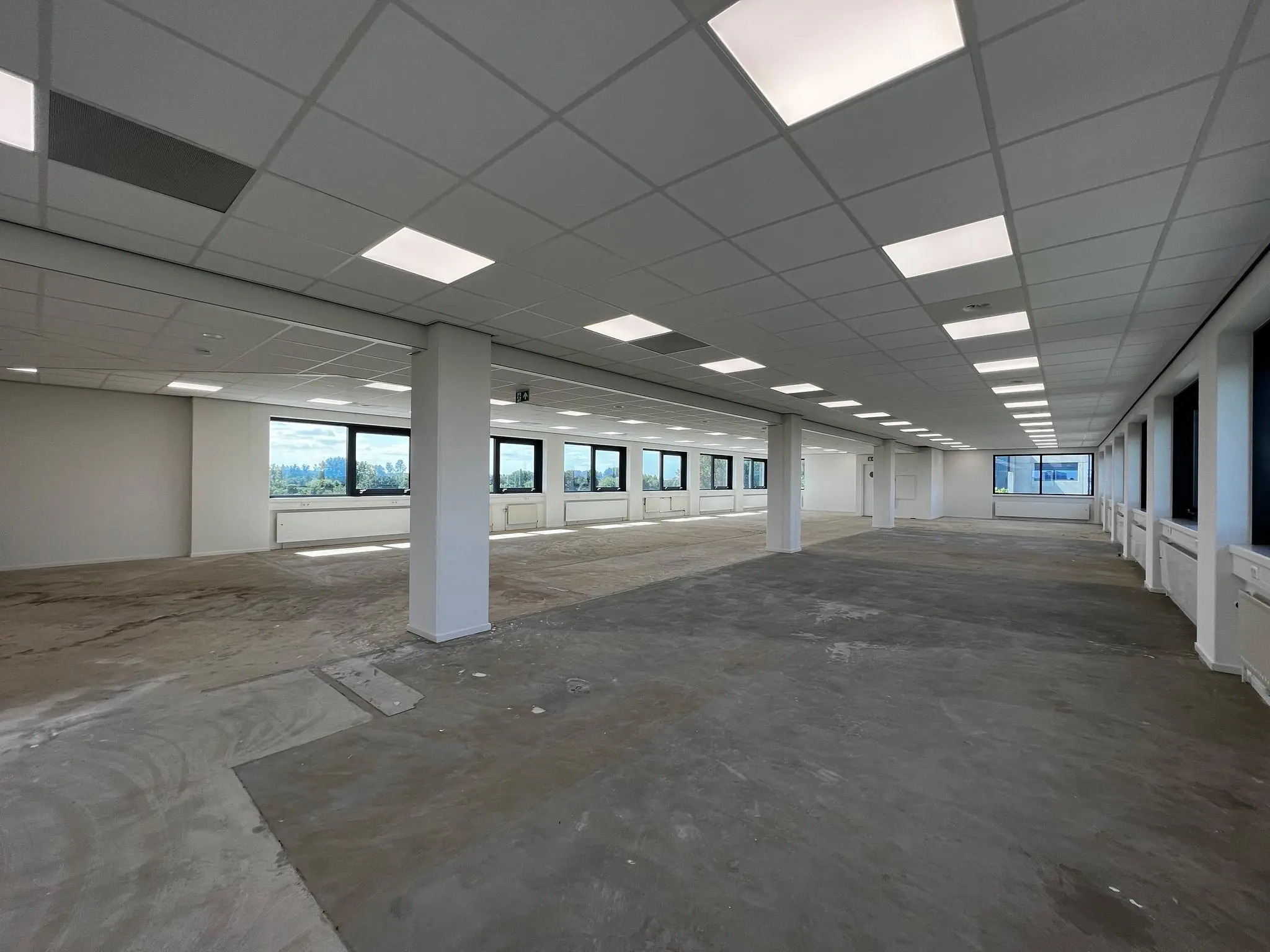 Leeg kantoorpand aan de Nevelgaarde met systeemplafond, grote ramen en onafgewerkte vloer.