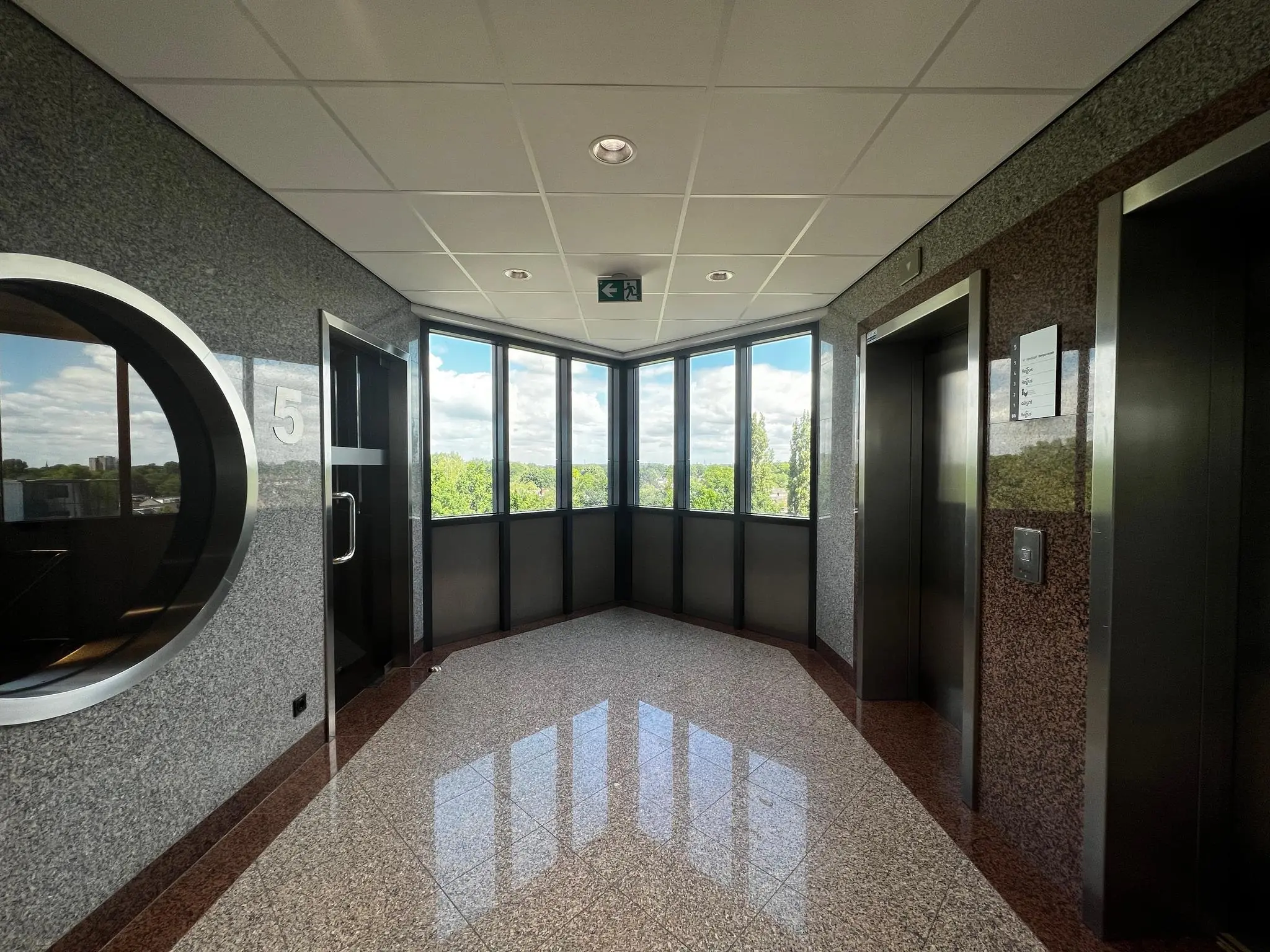 Licht en modern ingericht trappenhuis of lifthal op de vijfde verdieping van gebouw Nevelgaarde met uitzicht op groen landschap.