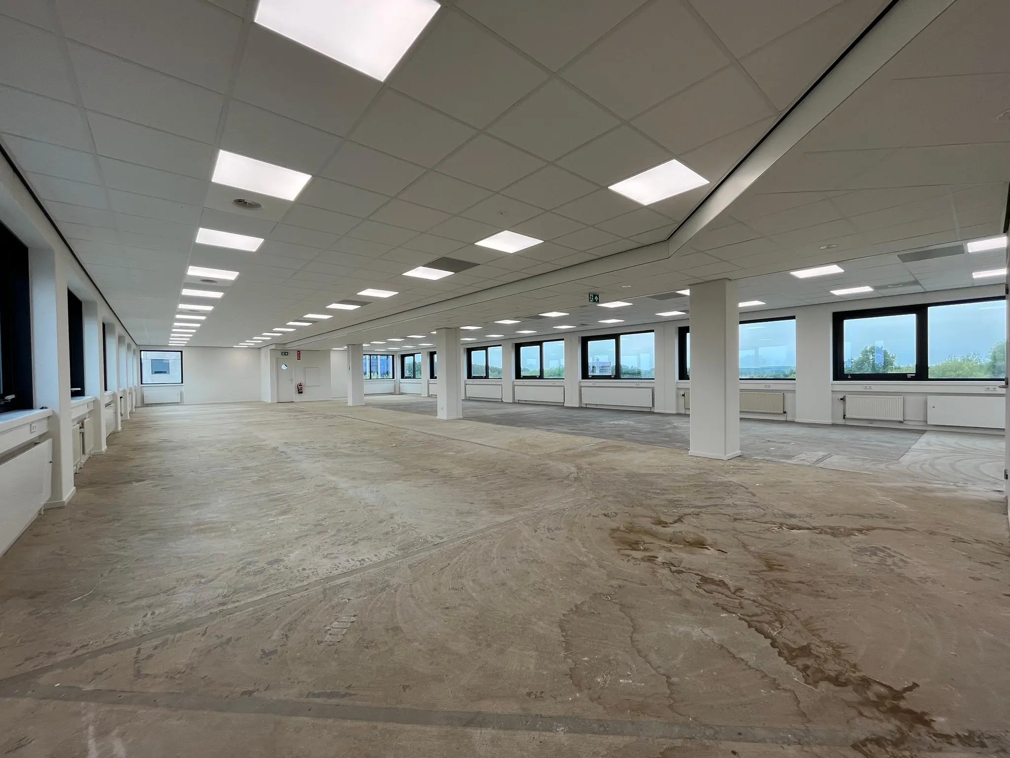 Leeg kantoorpand aan de Nevelgaarde met systeemplafond, betonnen vloer en grote ramen.