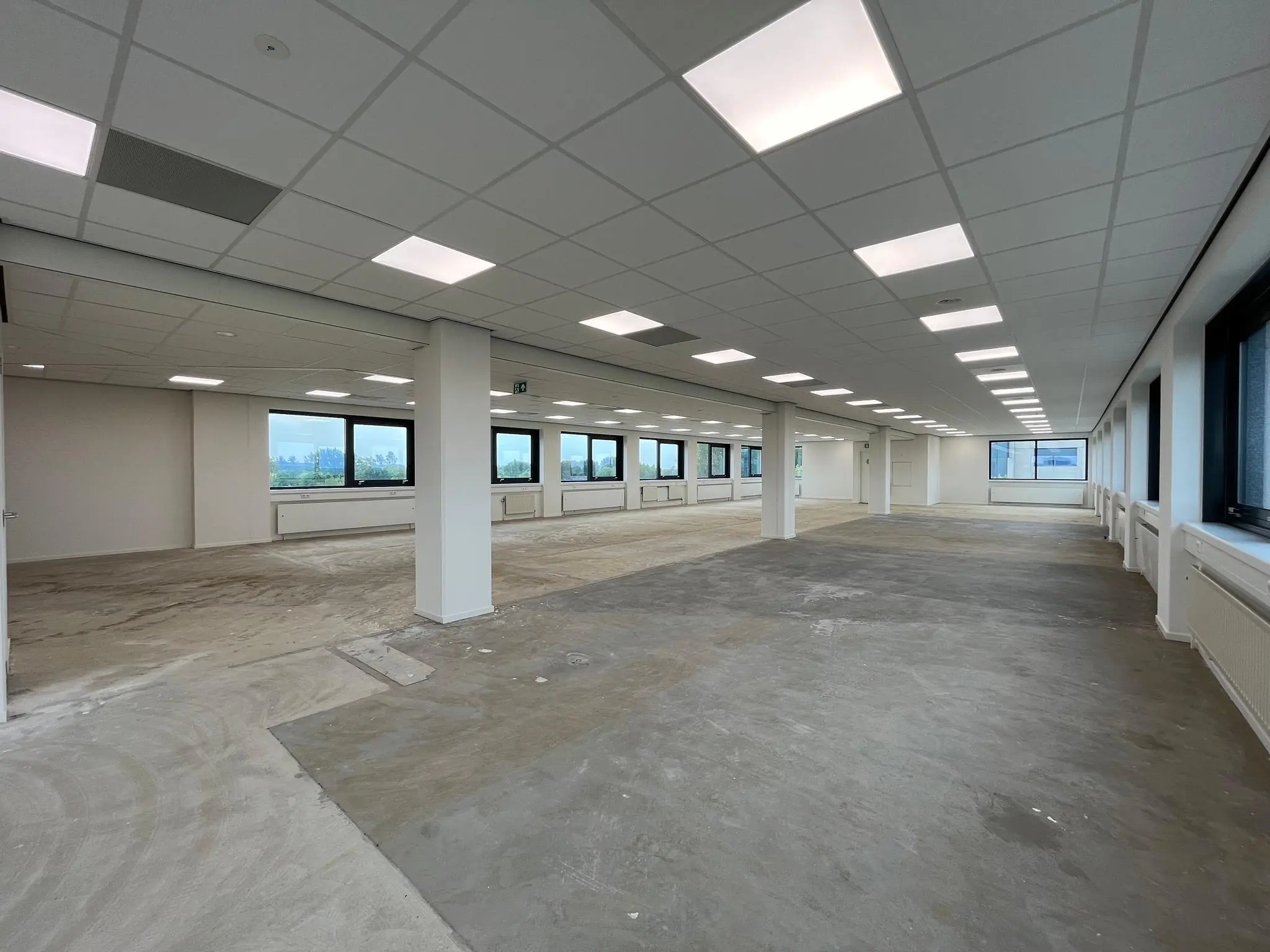 Leeg kantoorpand aan de Nevelgaarde met systeemplafond, grote ramen en onafgewerkte vloer.
