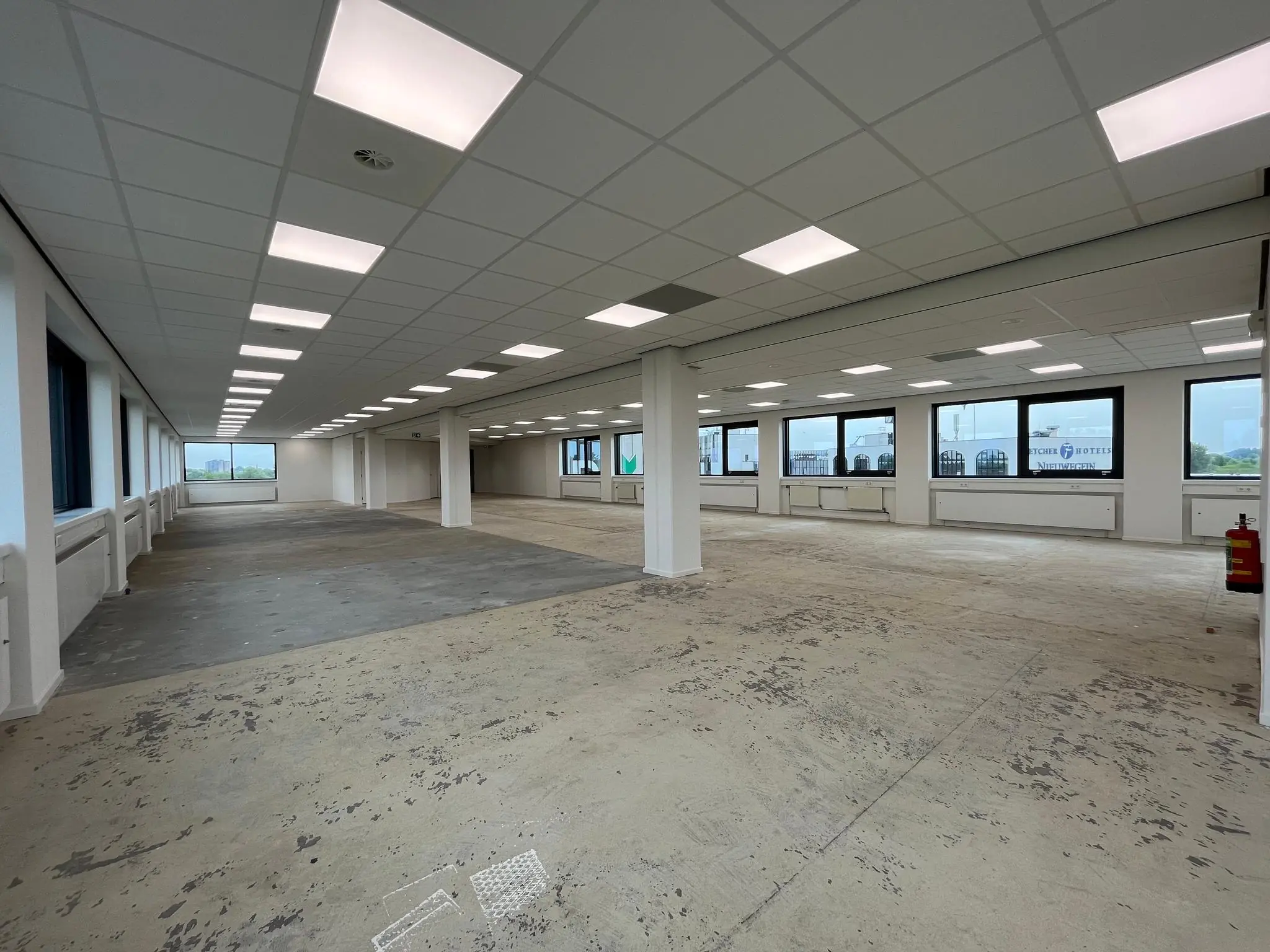 Leeg kantoorpand aan de Nevelgaarde met systeemplafond, grote ramen en onafgewerkte vloer.