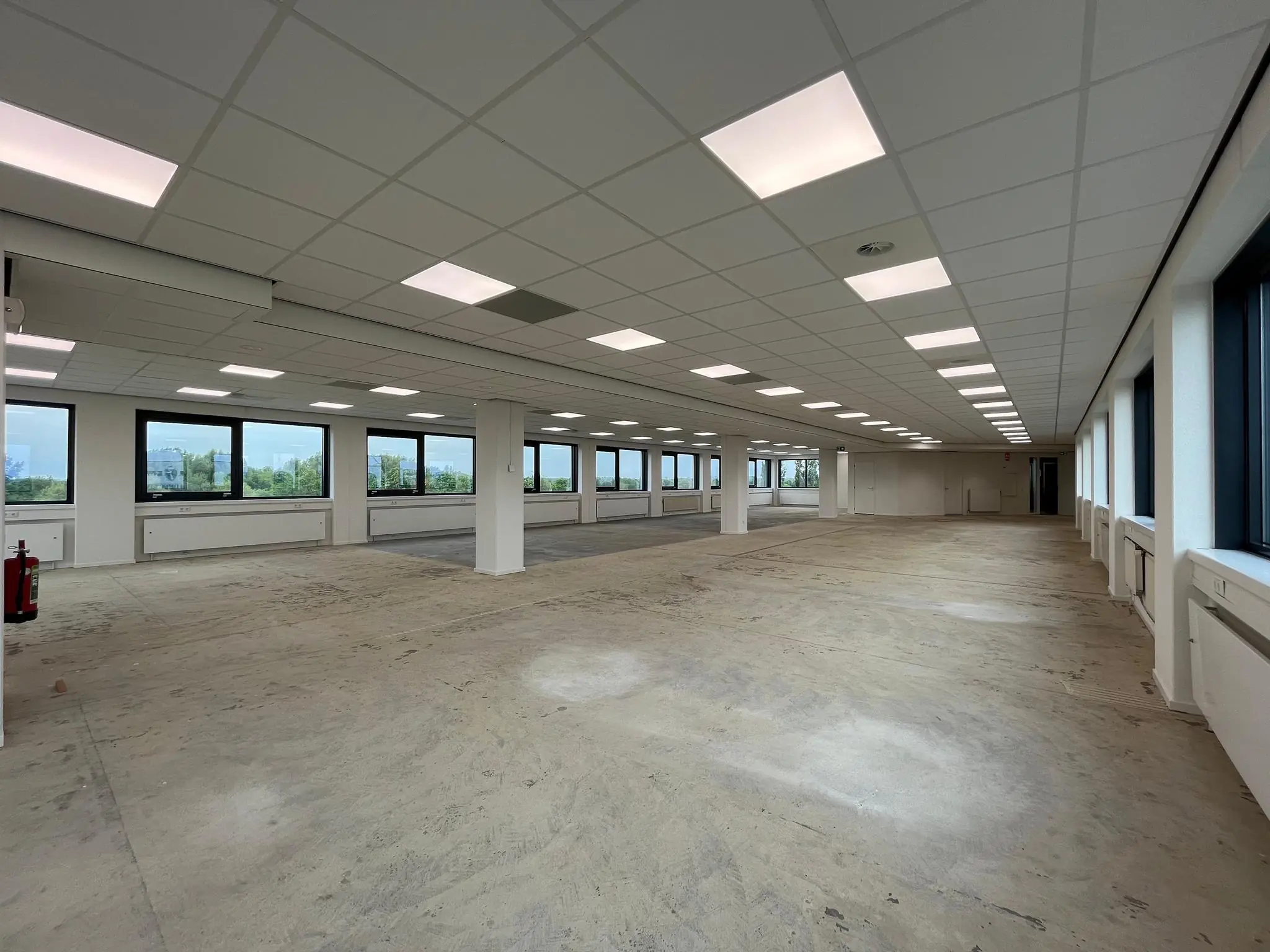 Leeg kantoorverdieping aan de Nevelgaarde met systeemplafond, grote ramen en betonnen vloer.