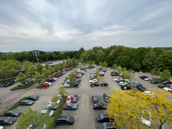 Overzicht van een parkeerplaats aan de Nevelgaarde, omgeven door bomen en geparkeerde auto's.