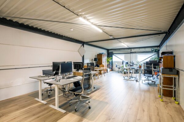 Modern ingericht kantoor aan de Aalsmeerderweg met meerdere werkplekken, bureaustoelen en computers op een lichte houten vloer.