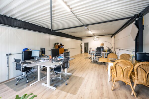 Moderne kantoorruimte aan de Aalsmeerderweg met bureaus, computers en een vergadertafel met rotan stoelen.