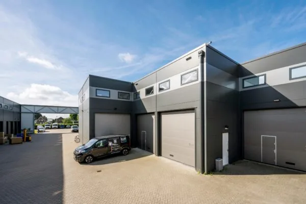 Modern bedrijfsverzamelgebouw aan de Aalsmeerderweg met meerdere garageboxen en geparkeerde bedrijfswagens.