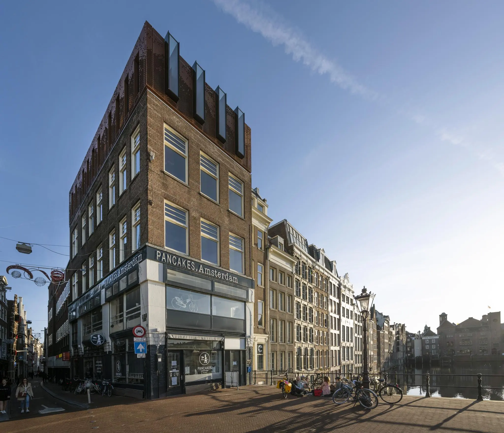 Straatbeeld van de Prins Hendrikkade in Amsterdam met het bakstenen hoekpand waarin PANCAKES Amsterdam is gevestigd, aan het water.