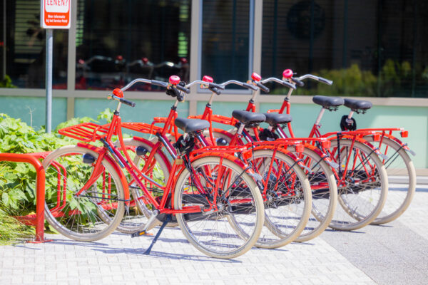 Rij felrode deelfietsen in een fietsenrek aan de Papendorpseweg bij een modern kantoorgebouw.