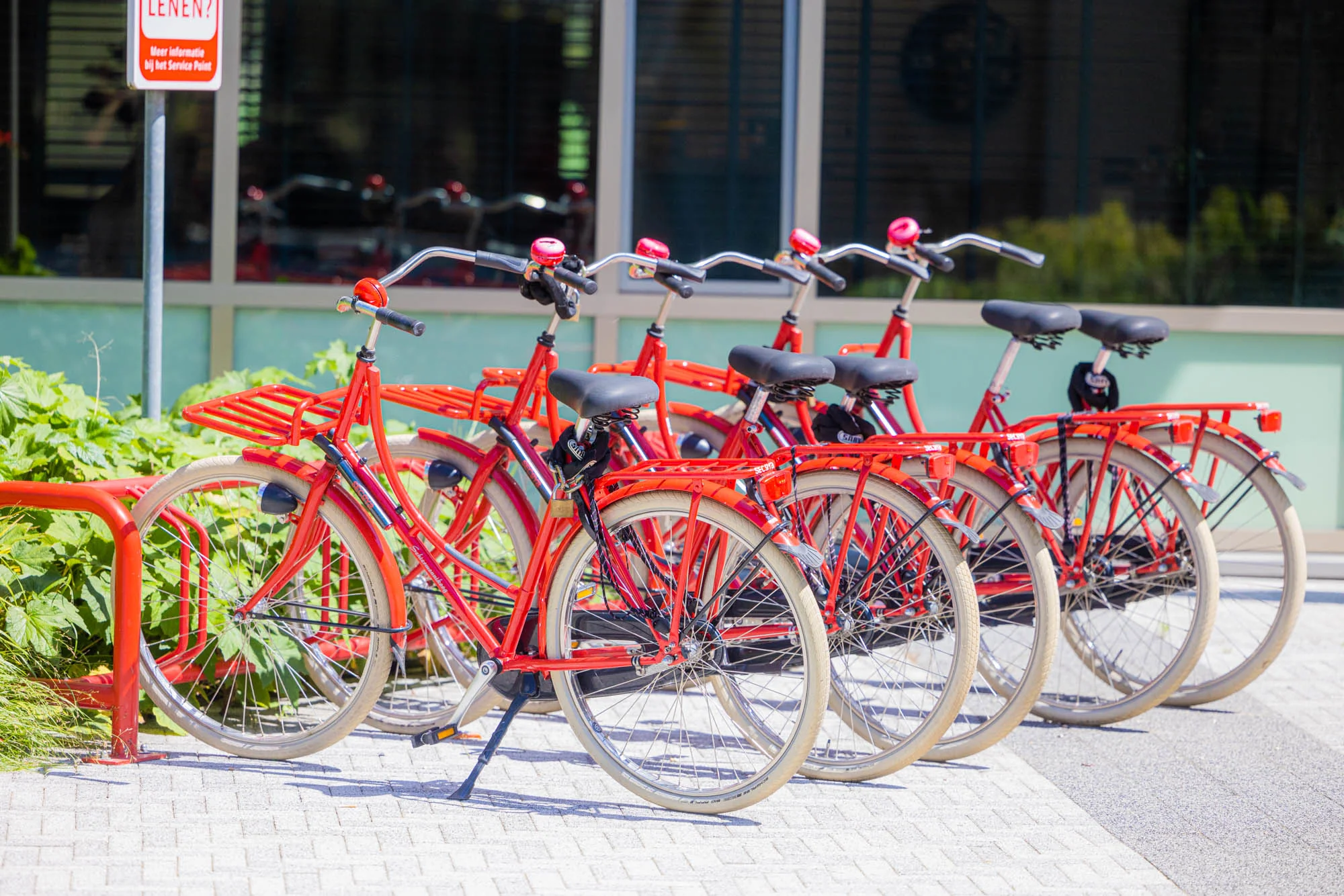 Rij felrode deelfietsen in een fietsenrek aan de Papendorpseweg bij een modern kantoorgebouw.