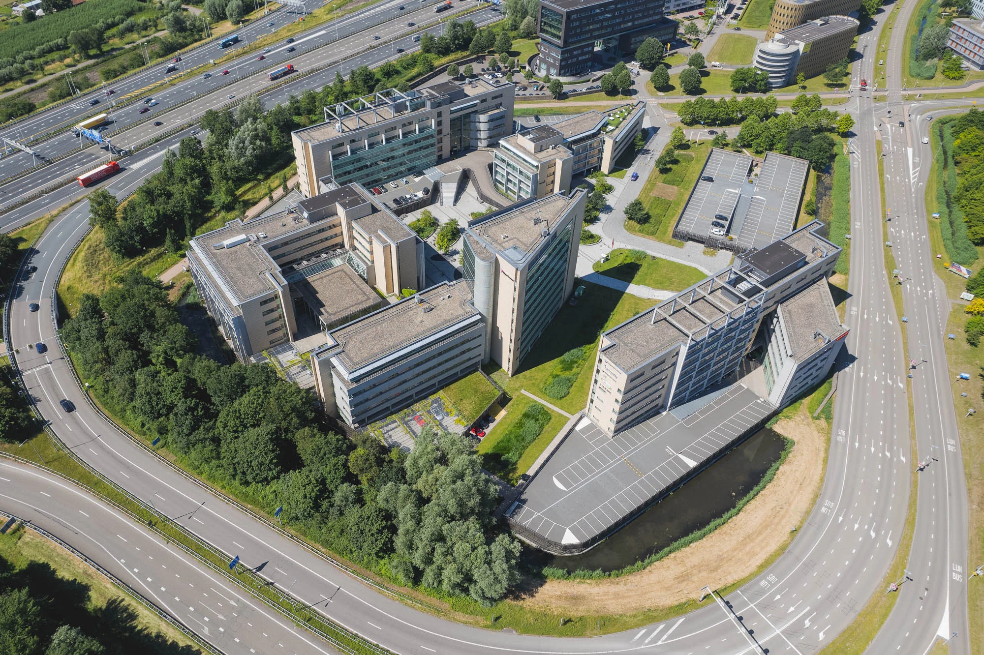 Luchtfoto van het kantoorgebouw aan de Papendorpseweg in Utrecht, omringd door snelwegen en parkeerplaatsen.