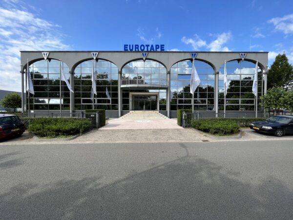 Vooraanzicht van het moderne kantoorpand van Eurotape aan de Oostergracht, met spiegelende ramen en witte vlaggen.