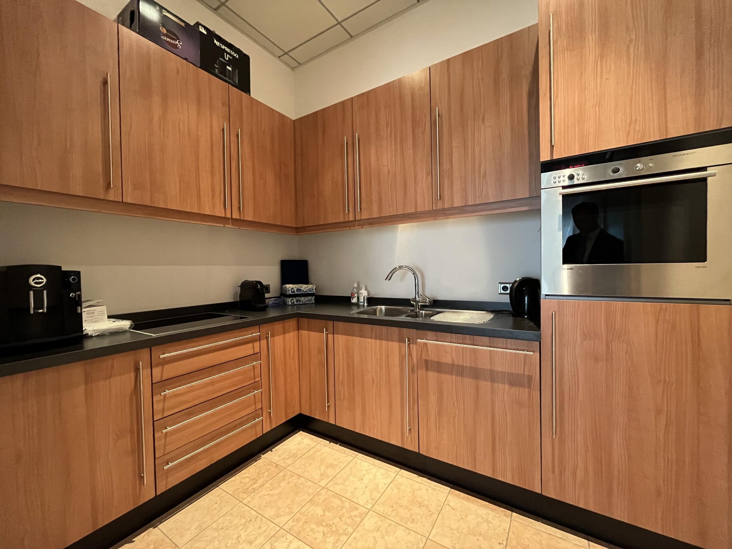 Moderne keuken met houten kasten, een ingebouwde oven en verschillende koffiezetapparaten.