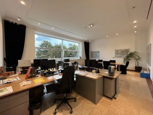 Modern kantoor aan de Oostergracht met meerdere bureaus, computers en grote ramen met uitzicht op bomen.