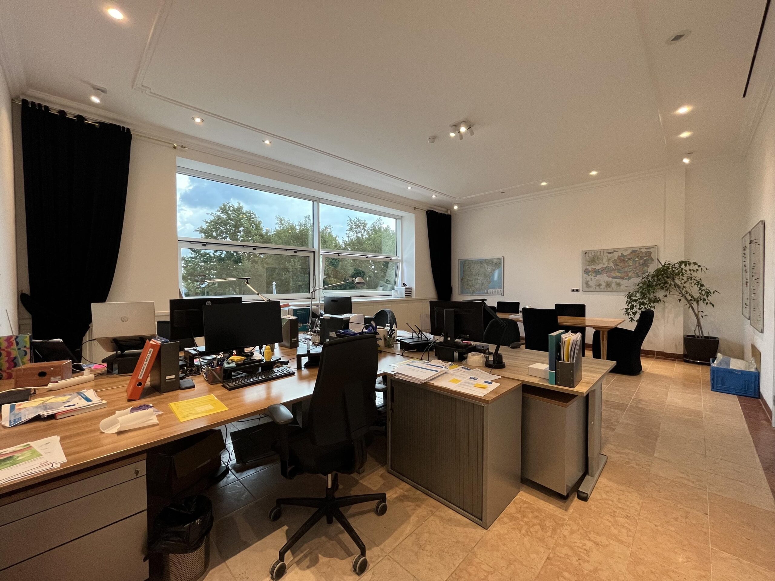 Een licht, ruim kantoor met meerdere bureaus, een grote raam en planten.