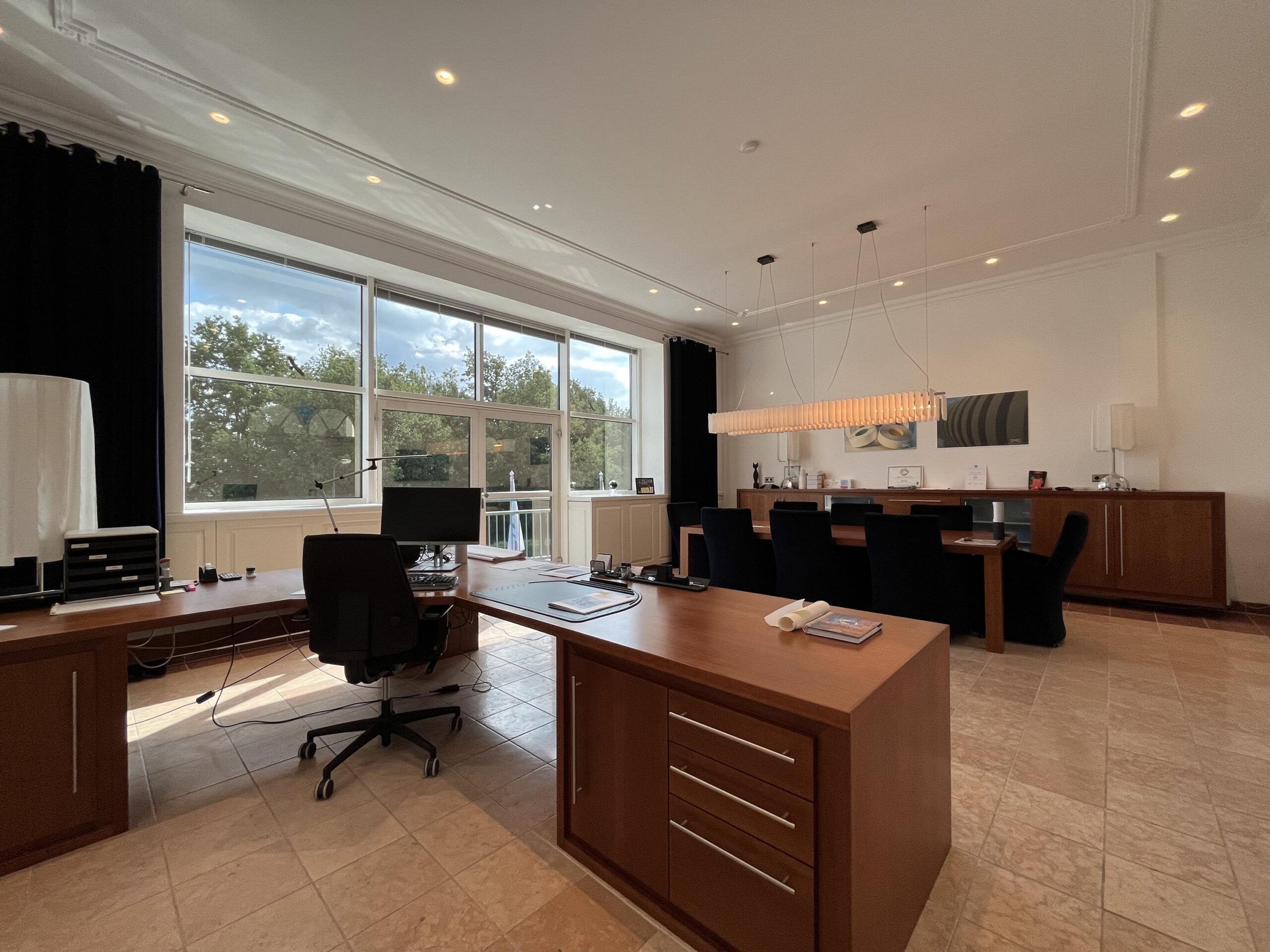 Een modern kantoor met grote ramen, houten meubels en een vergadertafel.