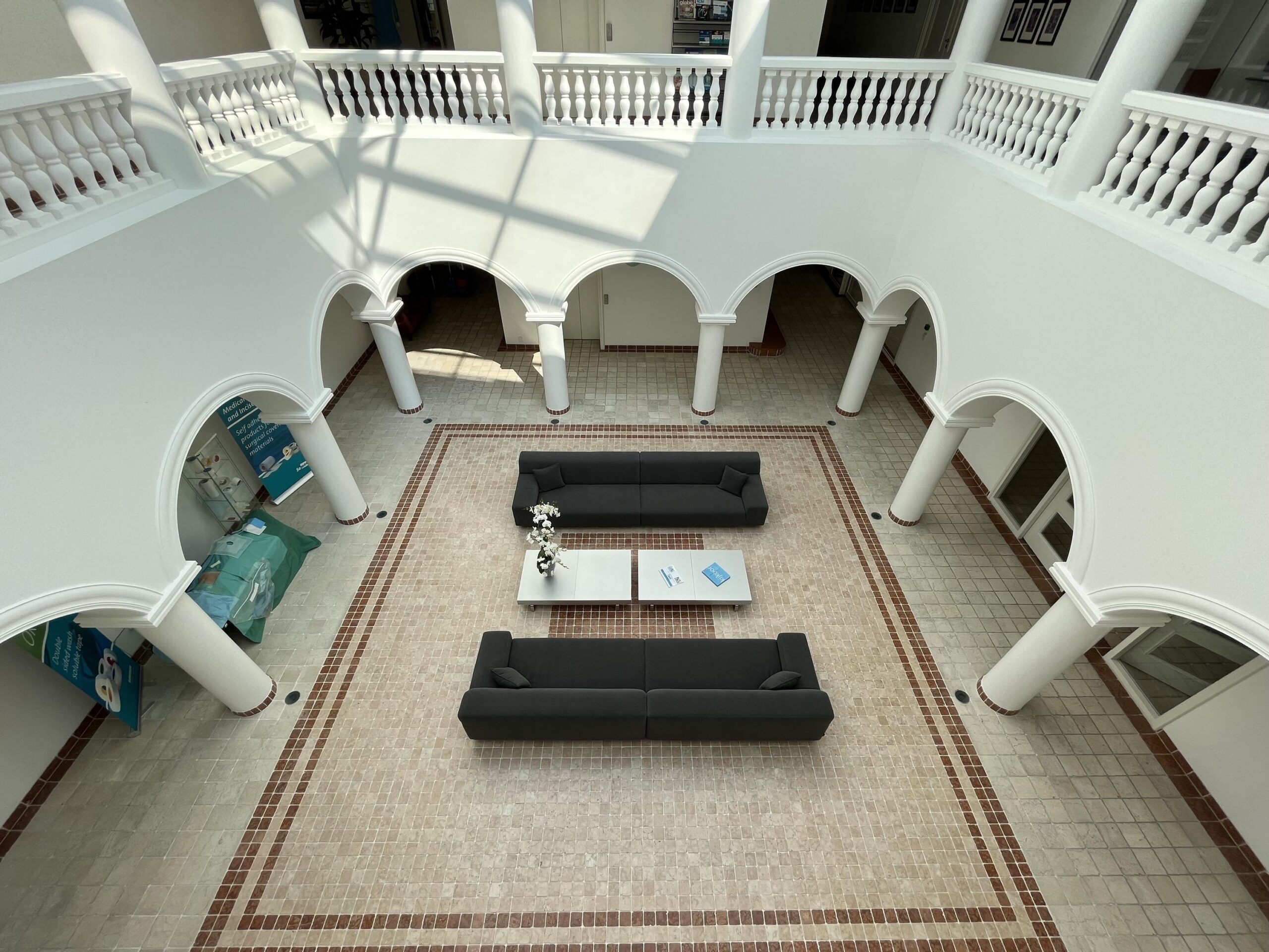 Een lichte, open binnenplaats met gewelfde witte muren, ingericht met grijze banken en een centrale tafel.