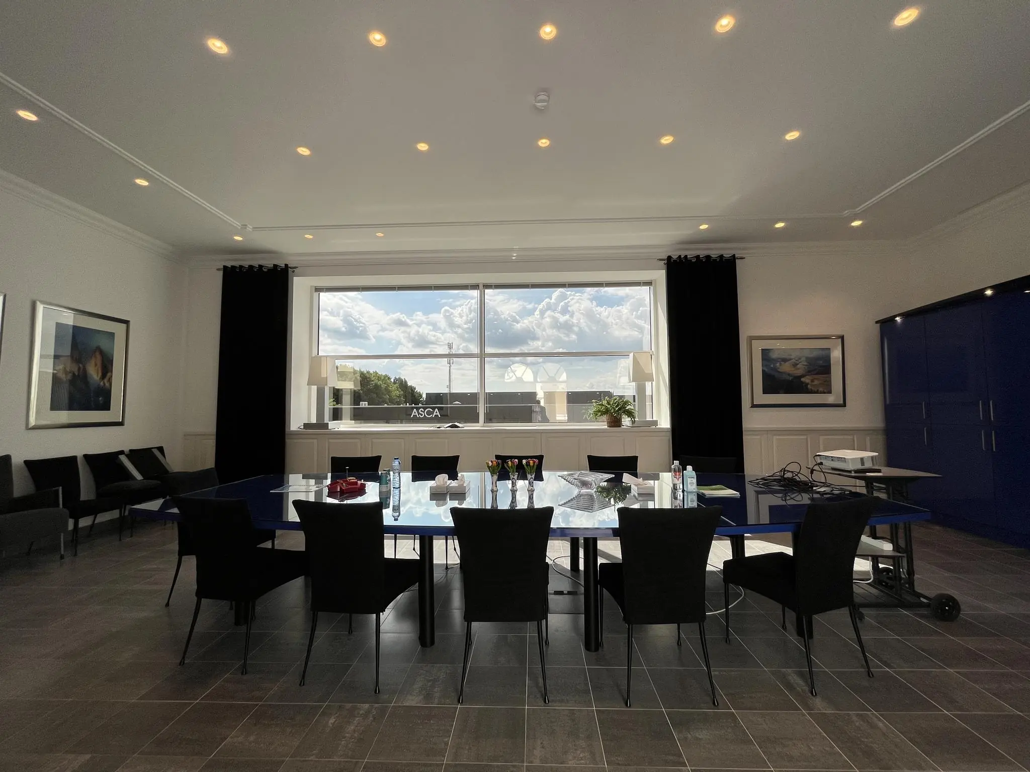 Vergaderruimte met grote tafel, zwarte stoelen, en een raam met uitzicht op het ASCA-pand aan de Oostergracht.