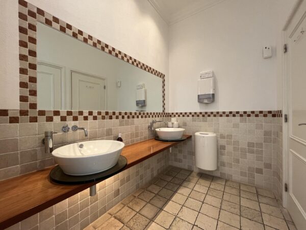 Moderne toiletruimte met twee waskommen op een houten blad, grote spiegel en beige tegelafwerking.