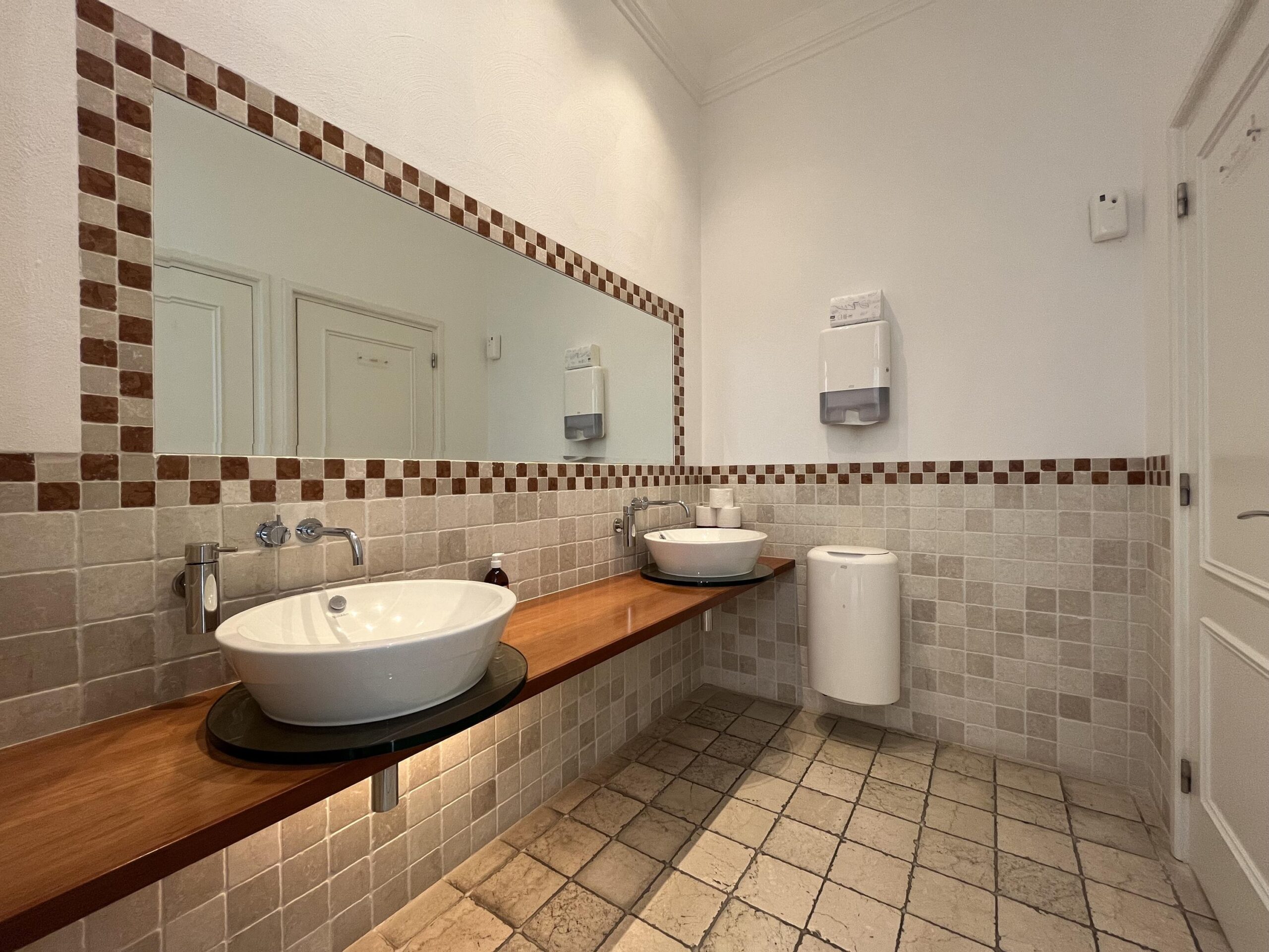 Badkamer met twee moderne wasbakken, een grote spiegel, en beige betegeling.