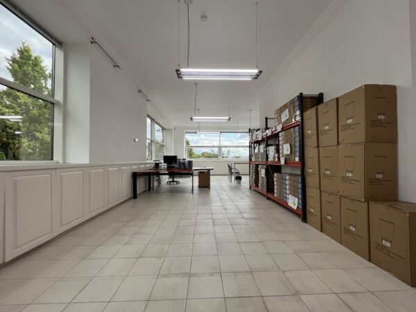 Ruim en licht kantoor- en opslagruimte aan de Oostergracht met bureaus, stellingen vol dozen en grote ramen.