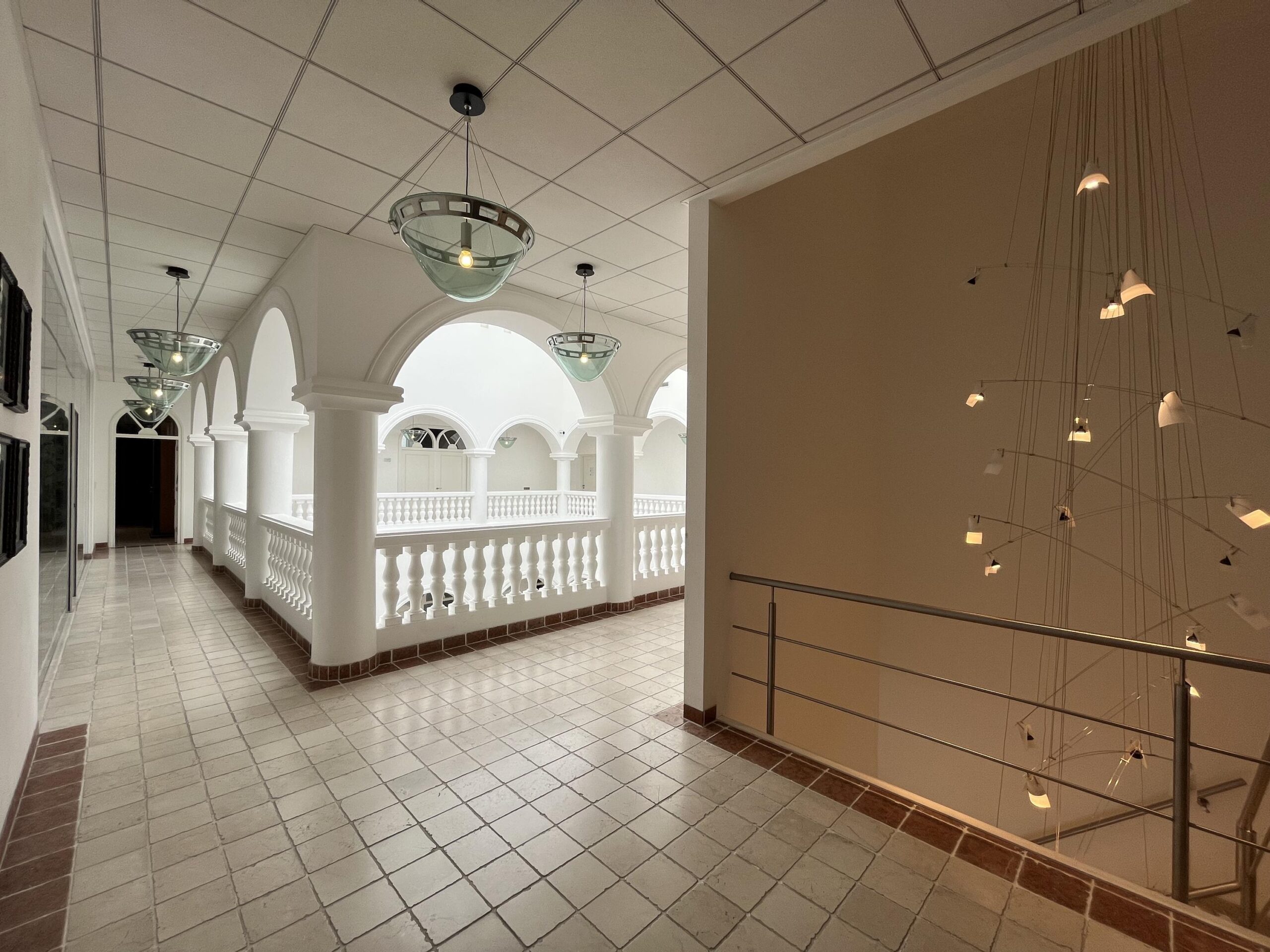 Een lichte gang met gebogen plafonds, witte balustrades en moderne hanglampen in het gebouw aan de Oostergracht.