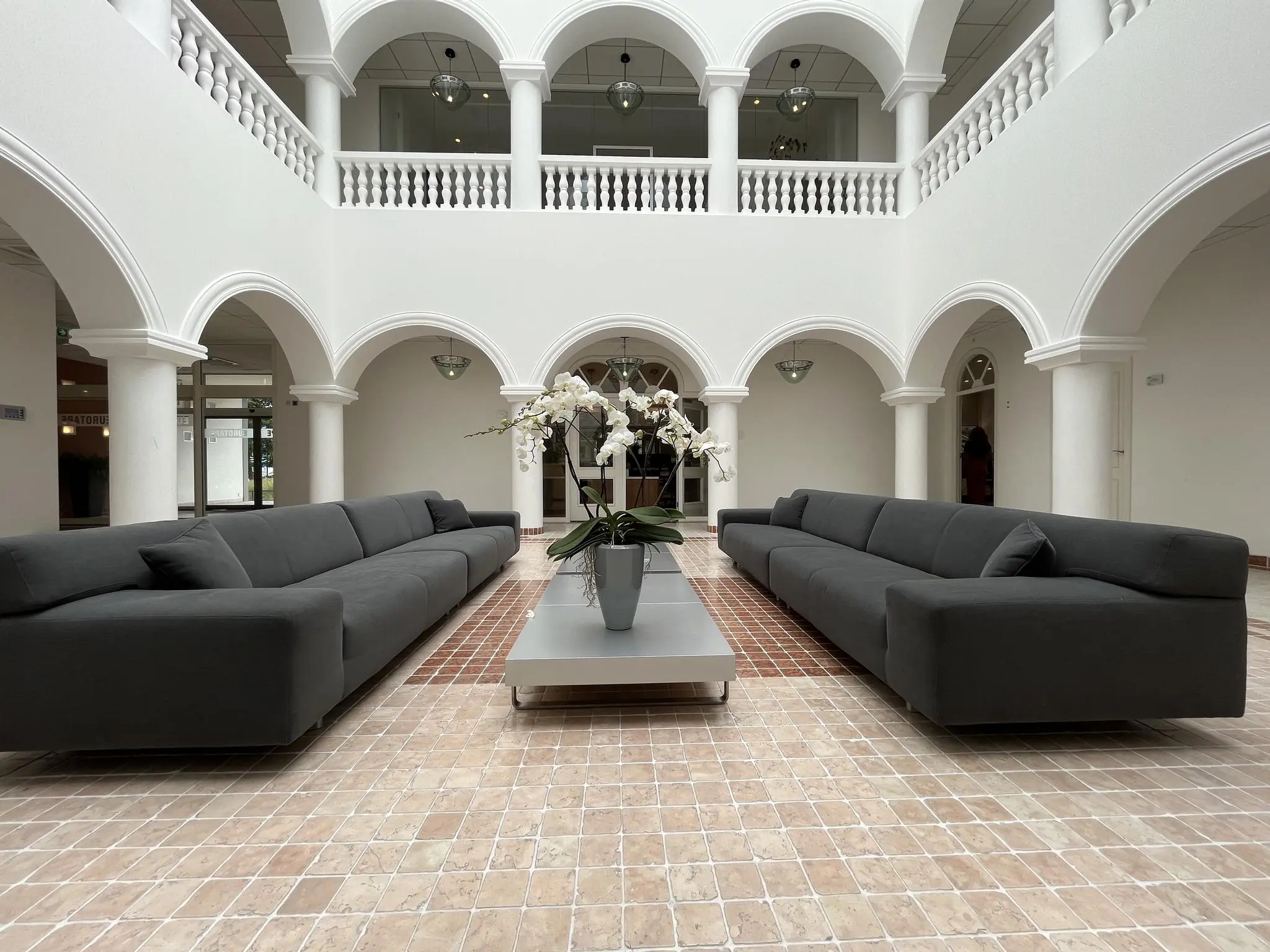 Moderne wachtruimte met twee lange, donkere banken, een lage tafel met een orchidee en omringd door witte zuilen en bogen in een gebouw aan de Oostergracht.