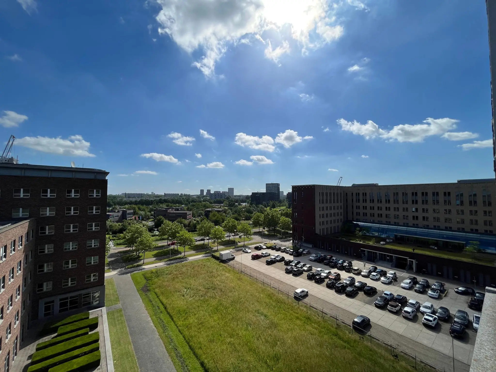Luchtfoto van de Orteliuslaan in Utrecht met kantoorgebouwen, parkeerterrein en groene omgeving onder een heldere blauwe lucht.