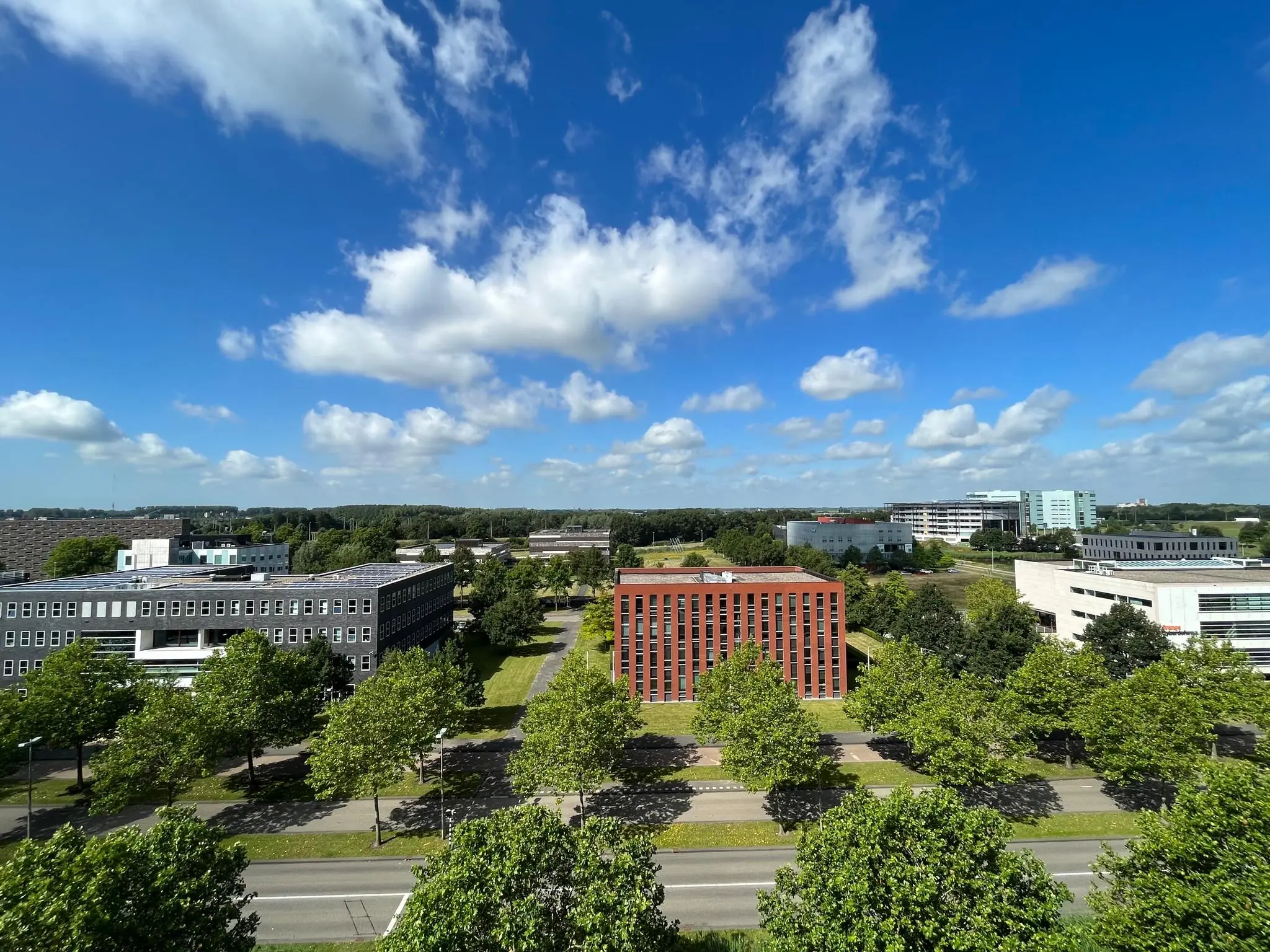 Luchtfoto van kantoorgebouwen aan de Orteliuslaan in Utrecht, omgeven door groene bomen en een blauwe lucht met wolken.