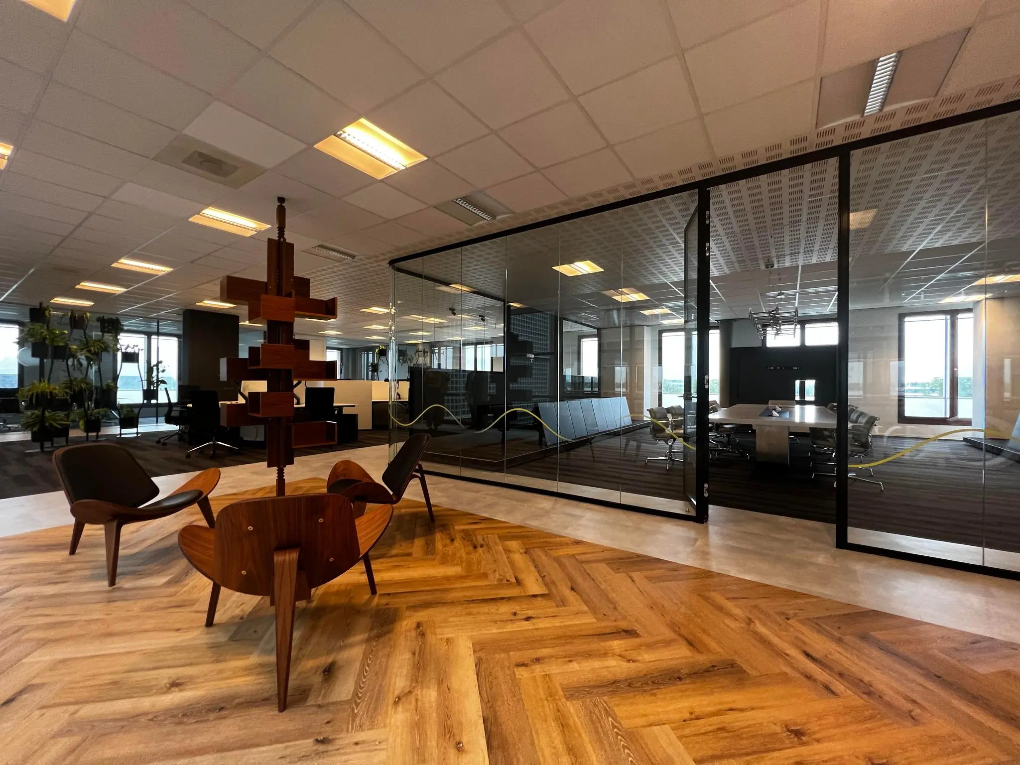 Modern kantoorinterieur aan de Hondiuslaan met glazen vergaderruimte en zithoek met houten stoelen.