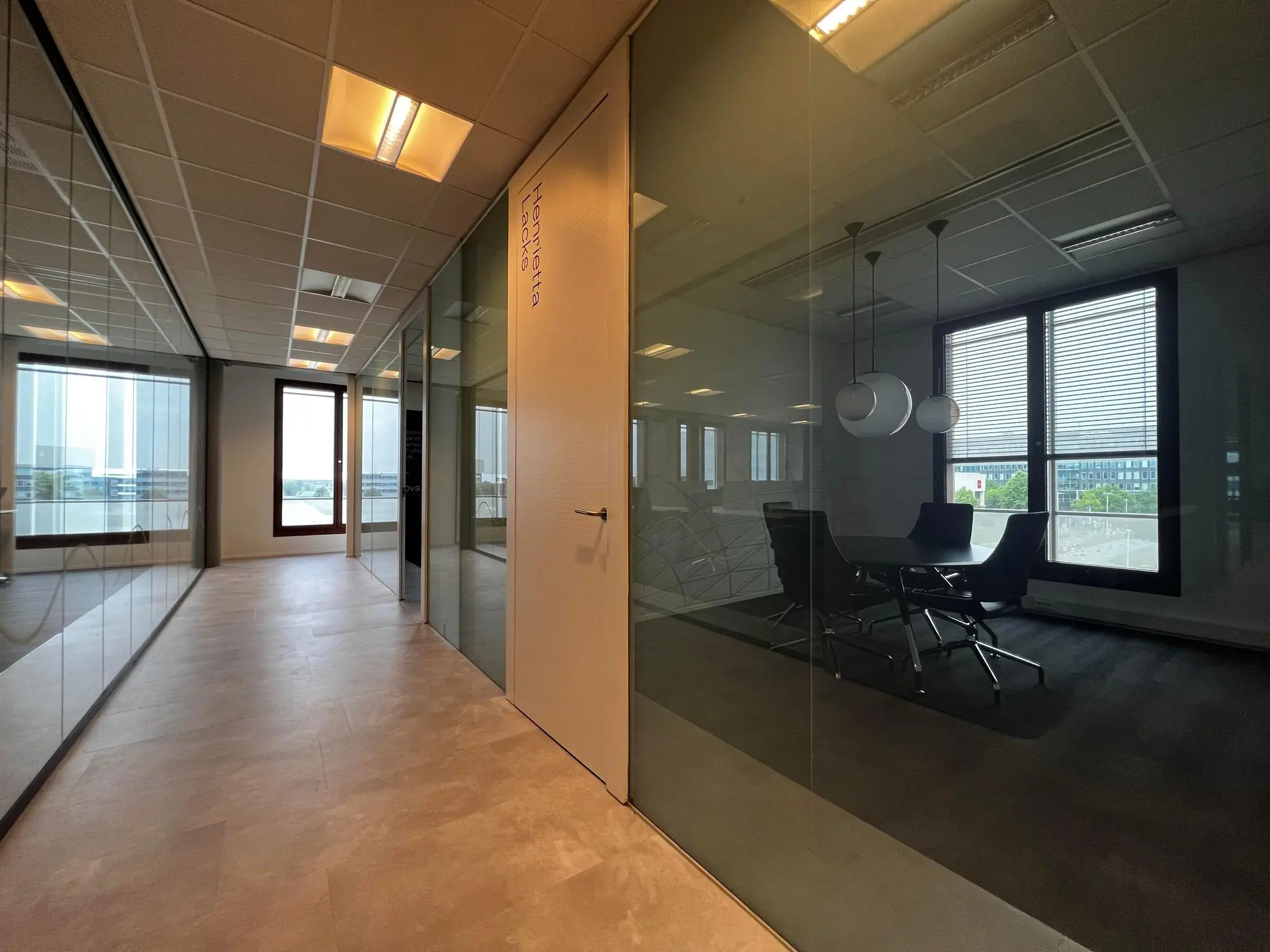 Moderne kantoorgang aan de Hondiuslaan met glazen wanden en zicht op vergaderruimte.