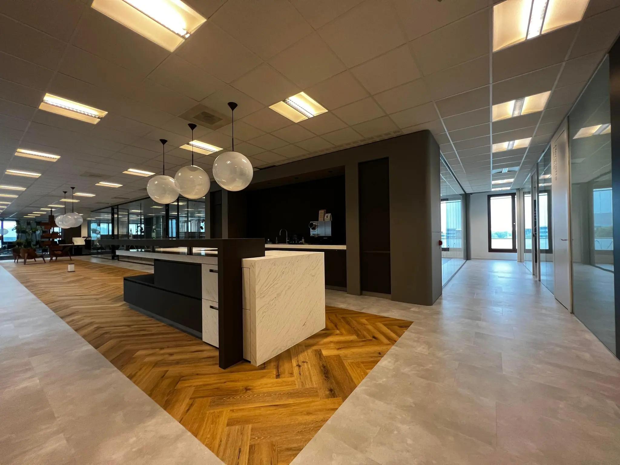 Moderne kantoorpresentatie aan de Hondiuslaan met open werkruimte, glazen wanden en centraal keukeneiland met hanglampen.