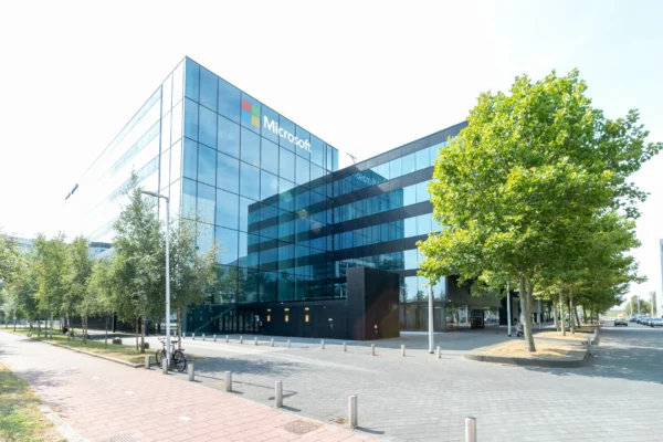 Modern kantoorgebouw met een Microsoft-logo op de gevel, omringd door bomen en een fiets op de stoep.