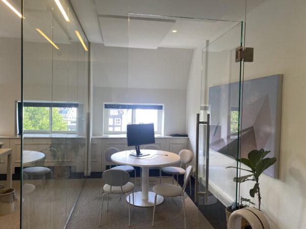 Moderne vergaderruimte aan de Herengracht met ronde tafel, vier stoelen, computerscherm en glazen wanden.