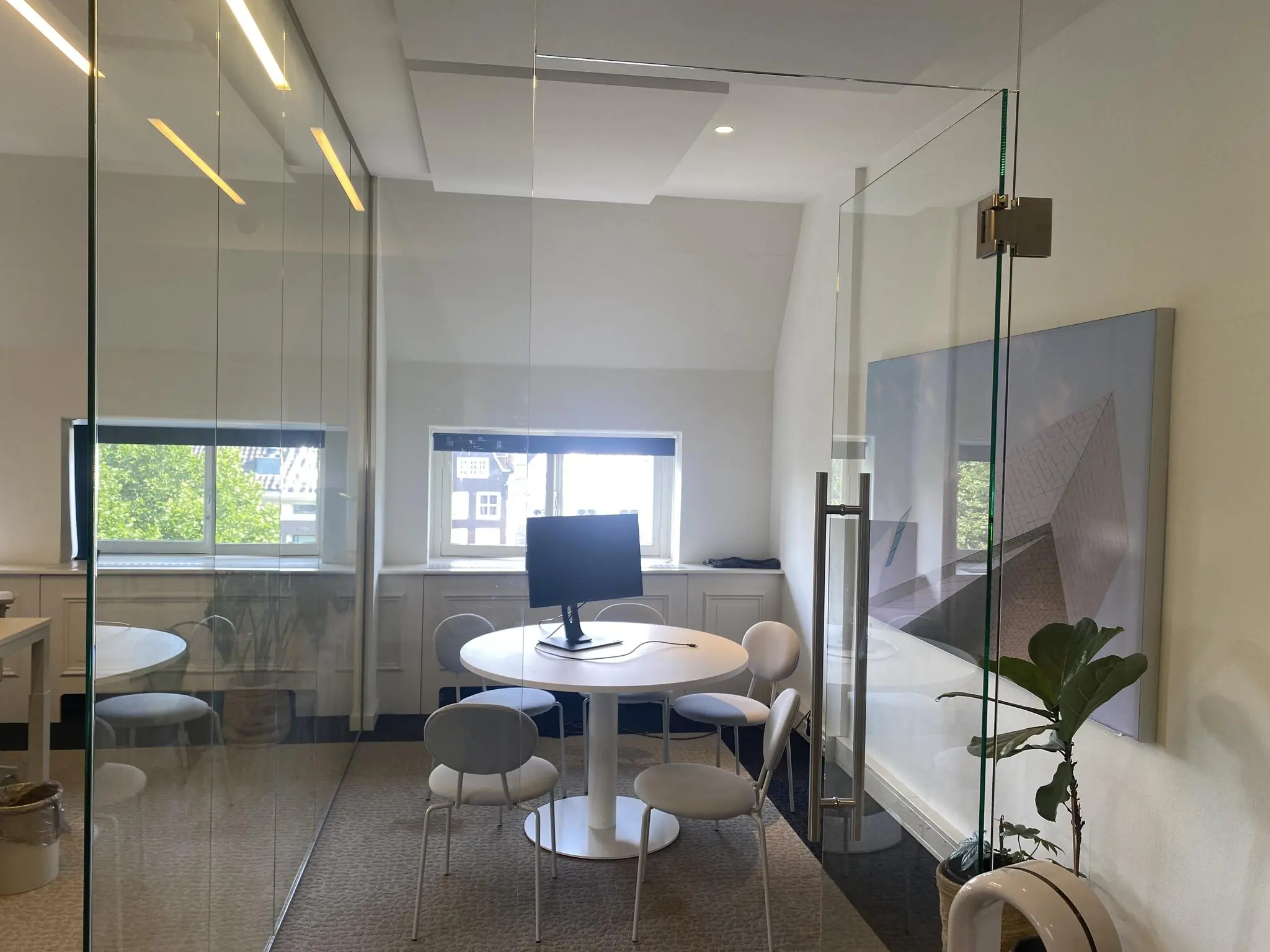 Moderne vergaderruimte aan de Herengracht met ronde tafel, vier stoelen, computerscherm en glazen wanden.