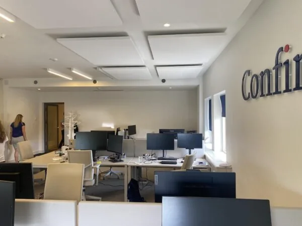 Moderne kantooruimte aan de Herengracht met werkplekken, computers en het bedrijfslogo "Confirm" op de muur.