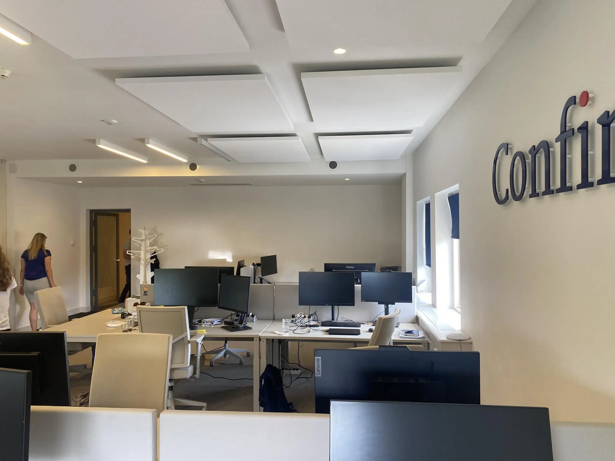 Moderne kantooruimte aan de Herengracht met werkplekken, computers en het bedrijfslogo "Confirm" op de muur.