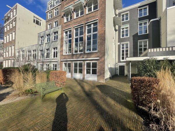 Binnenplaats met bakstenen bestrating en een groene bank, omringd door hoge gevels aan de Herengracht.