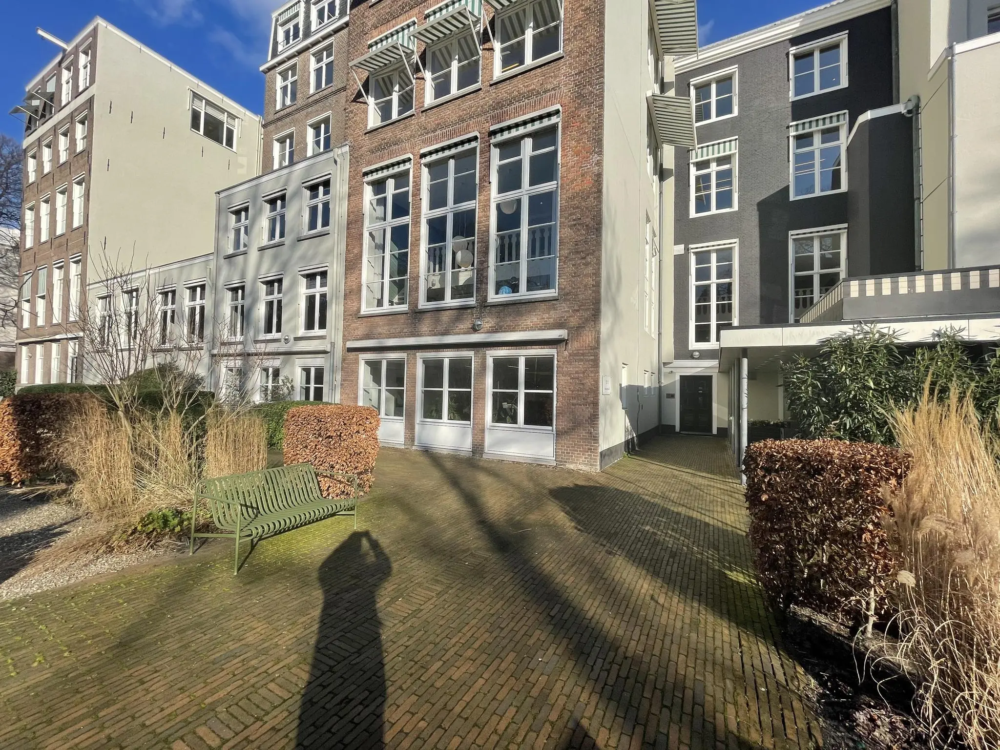 Binnenplaats met bakstenen bestrating en een groene bank, omringd door hoge gevels aan de Herengracht.