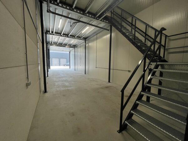 Interieur van een lege bedrijfsruimte aan de Aalsmeerderweg met metalen trap en open zicht naar de garagedeuren buiten.