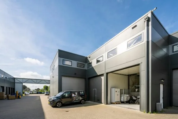 Moderne bedrijfsunits aan de Aalsmeerderweg met geopende overheaddeur en bedrijfswagens op het terrein.