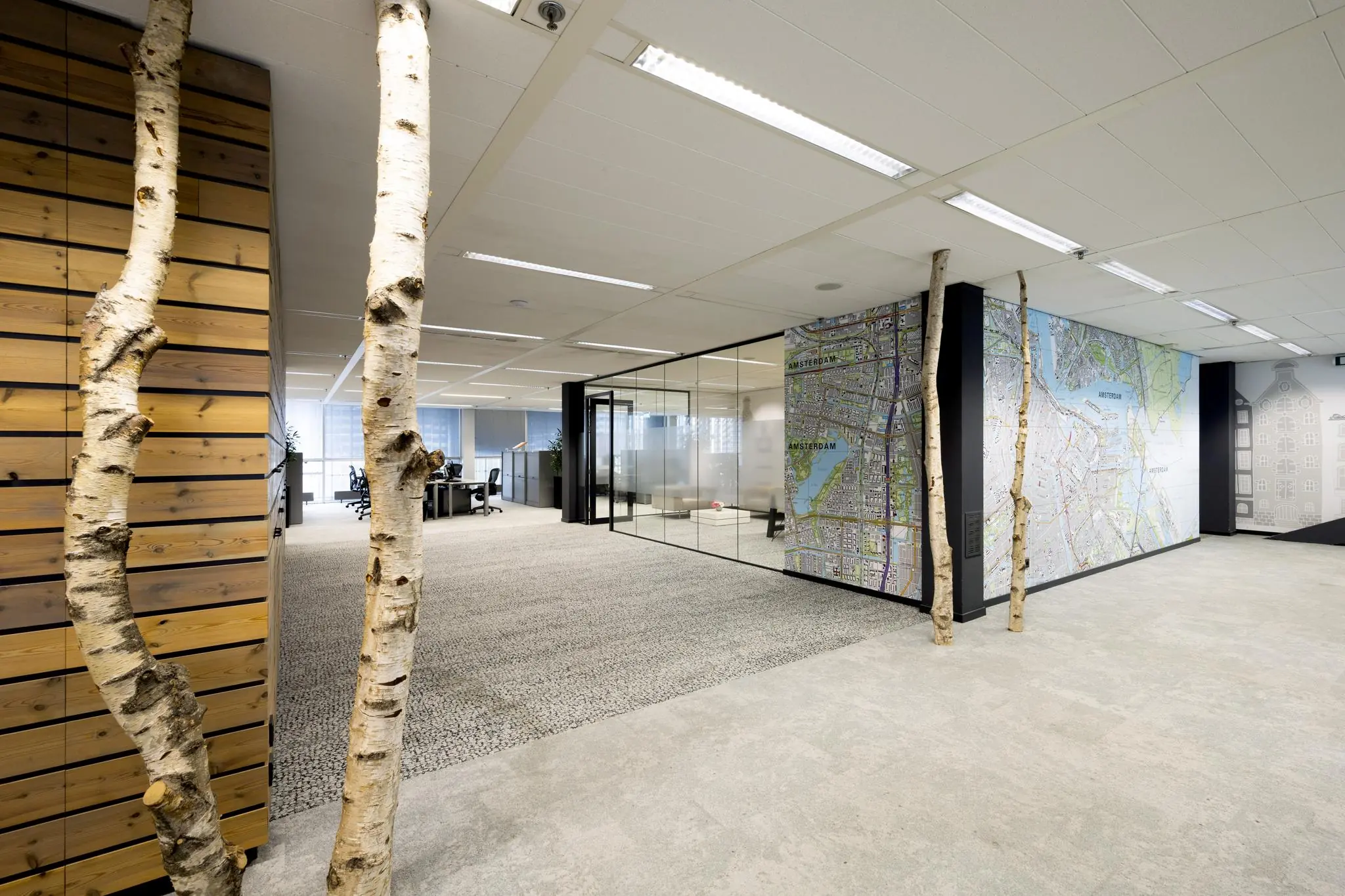 Modern kantoorinterieur aan de Jacob Bontiusplaats met glazen vergaderruimtes, boomstammen als decoratie en een grote kaart van Amsterdam op de muur.