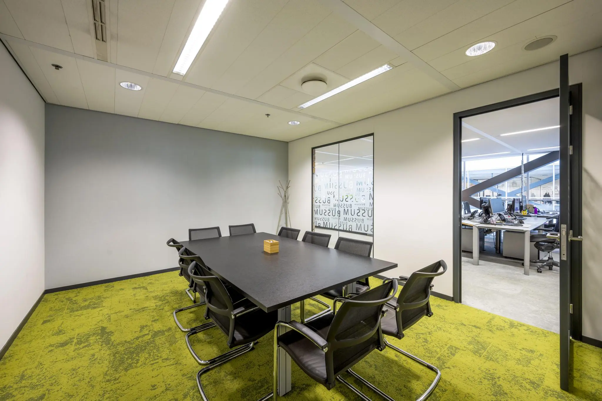 Vergaderruimte aan de Jacob Bontiusplaats met acht stoelen, een zwarte tafel en zicht op een aangrenzend kantoorgedeelte.