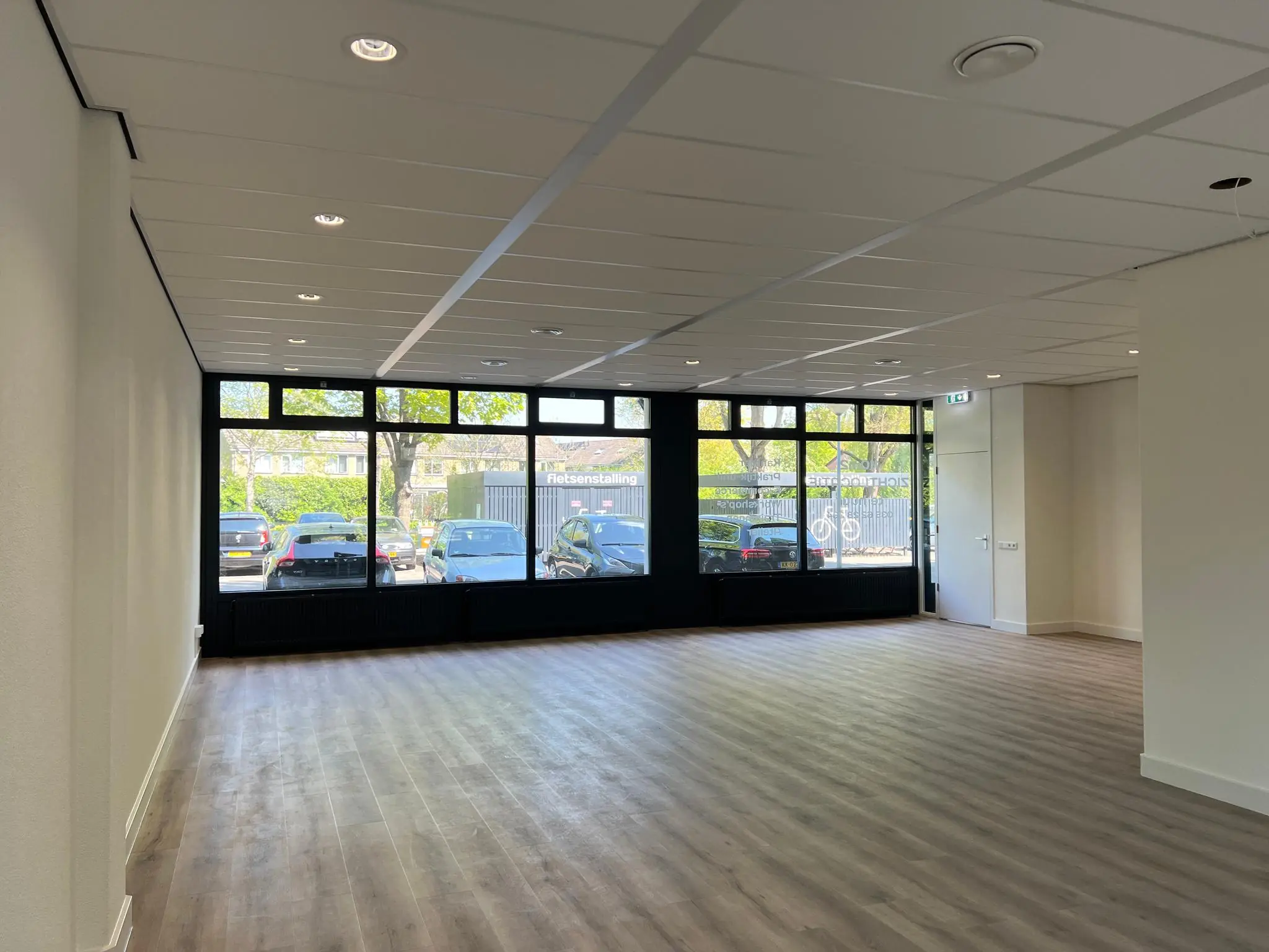 Lege, modern afgewerkte kantoor- of winkelruimte aan de Huizermaatweg met grote ramen en uitzicht op een parkeerplaats.
