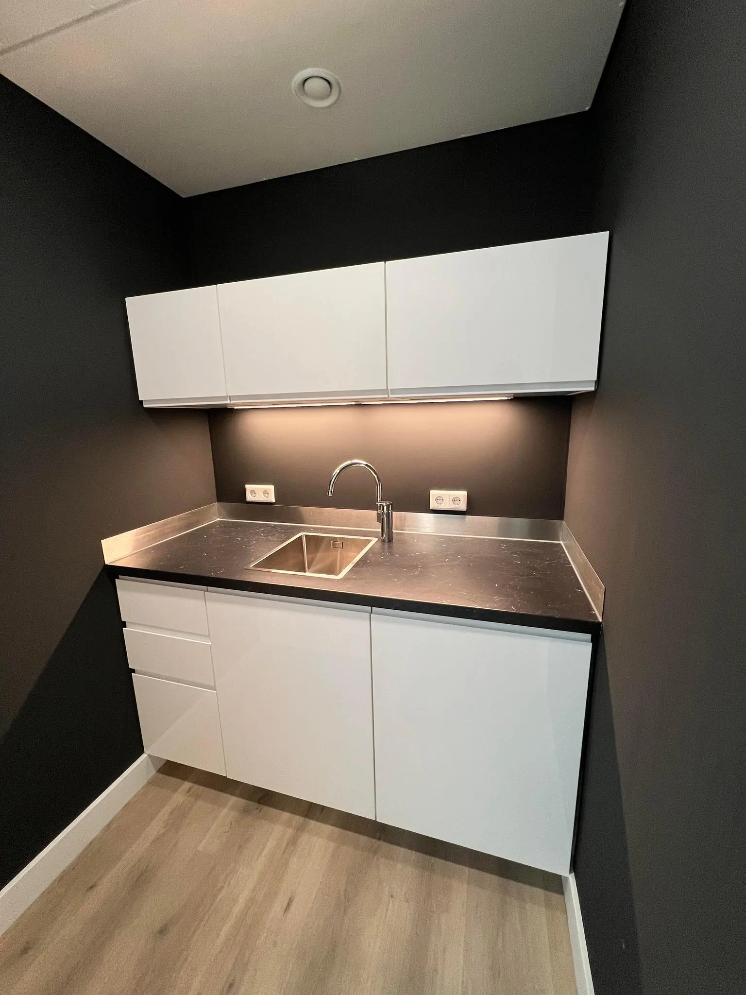 Moderne kitchenette aan de Huizermaatweg met zwarte muren, witte kasten en rvs spoelbak.