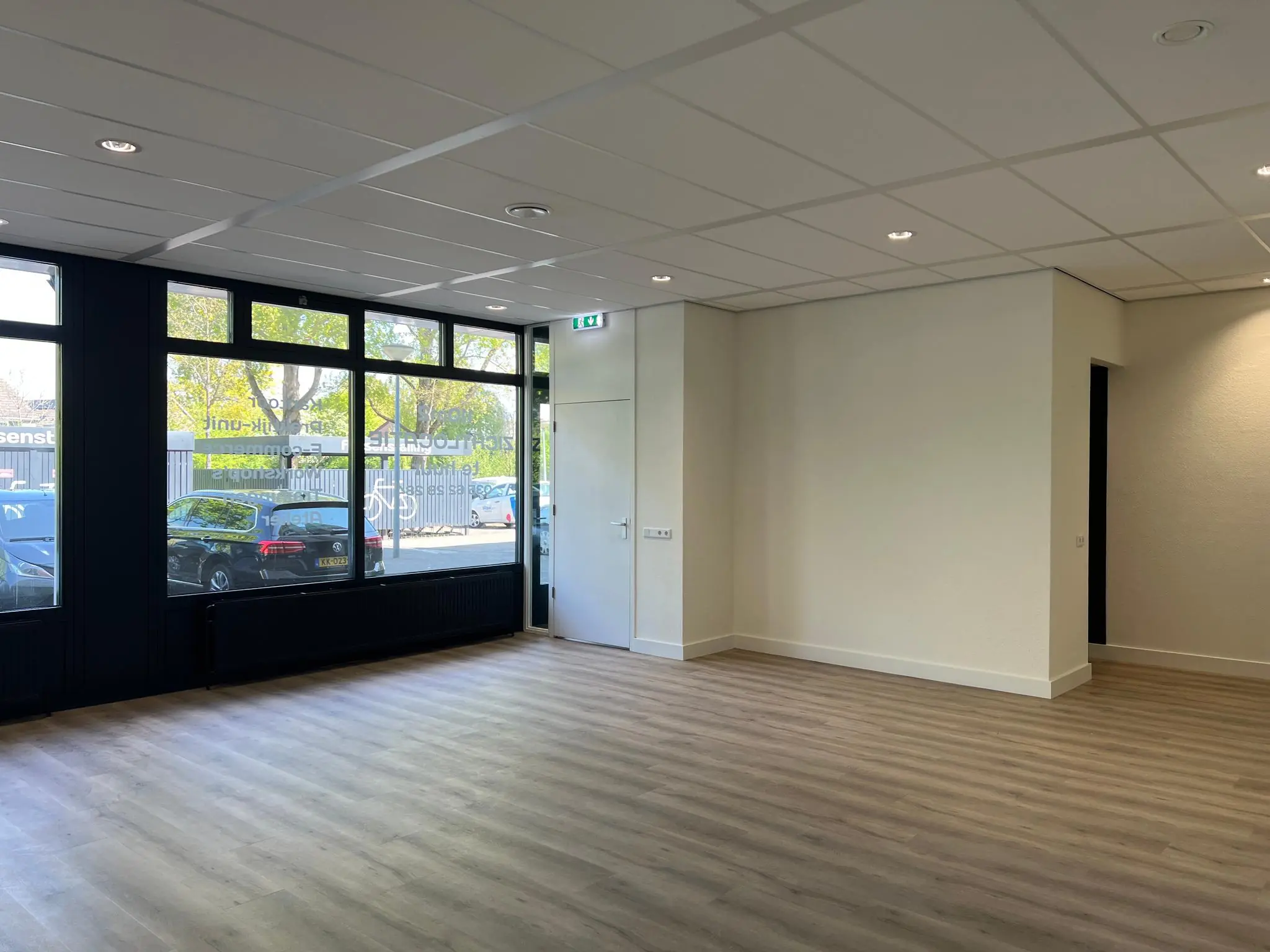 Lichte, lege kantoorruimte aan de Huizermaatweg met grote ramen en houten vloer.