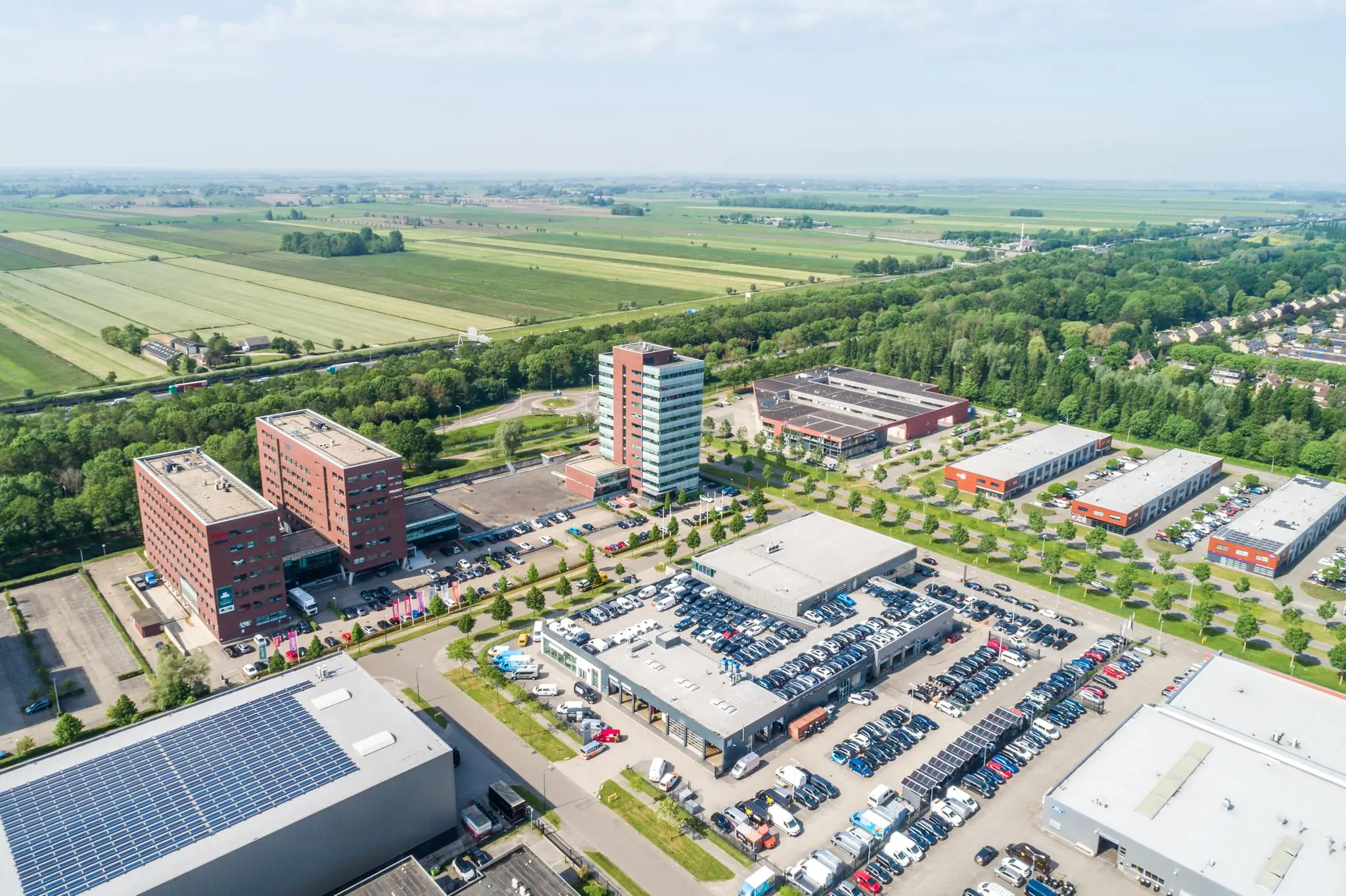 Luchtfoto van bedrijventerrein Rijnzathe met kantoorgebouwen, parkeerterreinen en omliggend groen landschap.