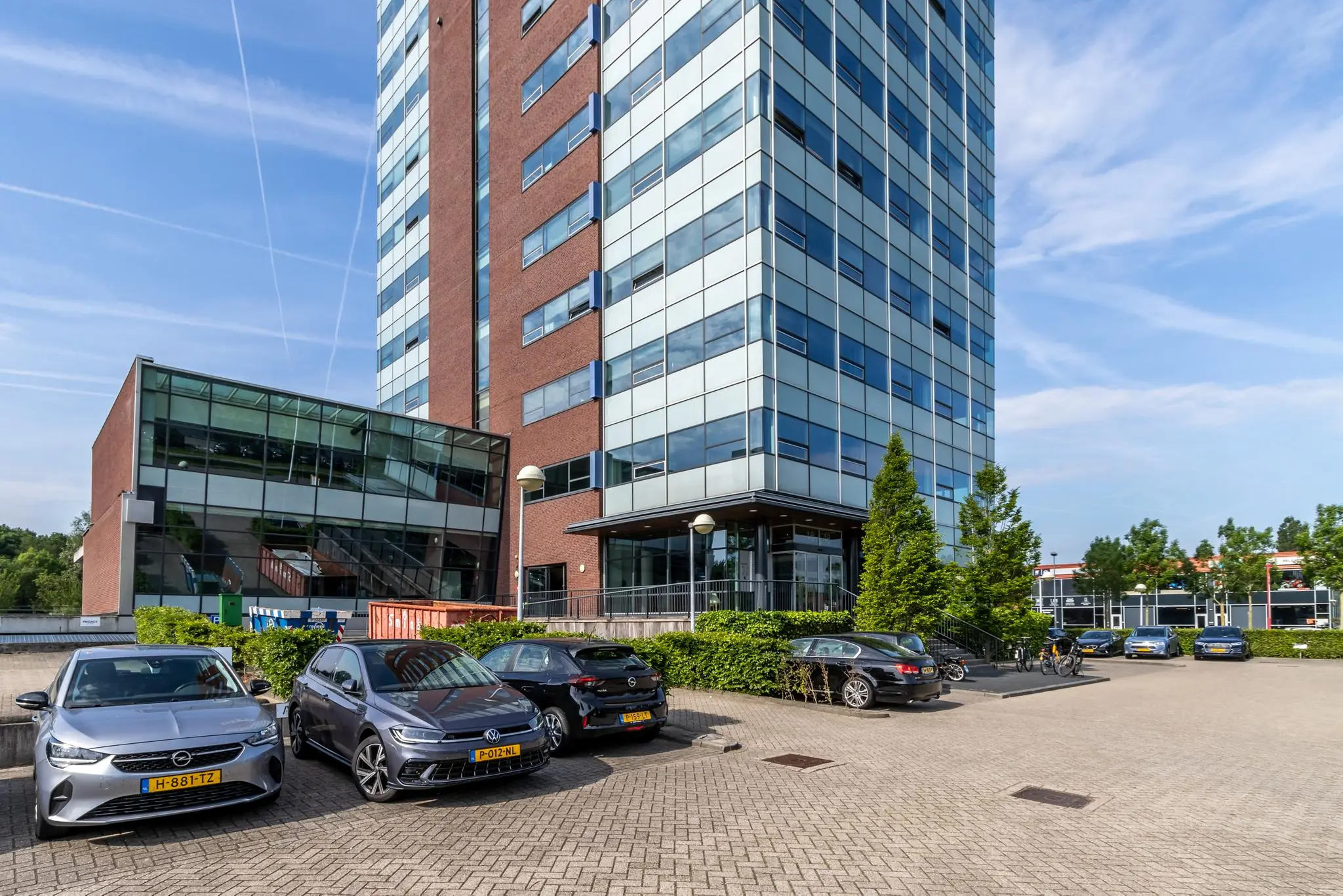 Kantoorgebouw Rijnzathe met aangrenzende parkeerplaats en geparkeerde auto's op een zonnige dag.